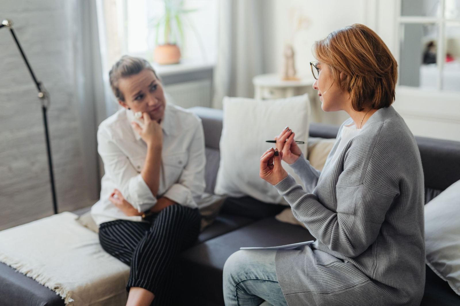 Two women sit on a sofa talking in a bright room