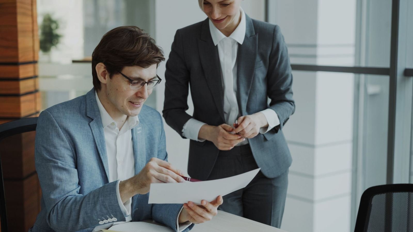 A man and a woman in business clothes look over a paper together in an office.