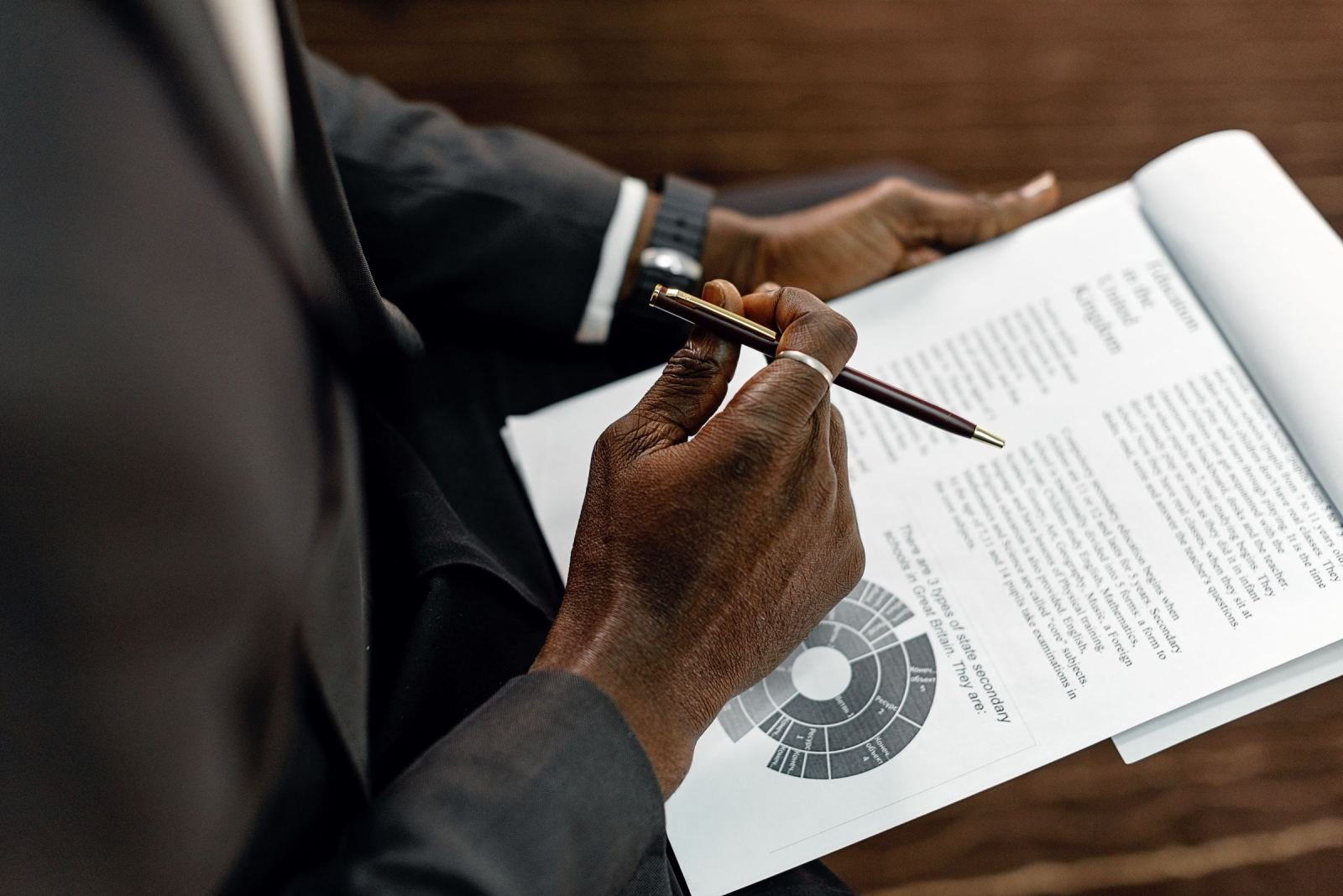 A person in a suit holds a pen over a document with a circular chart