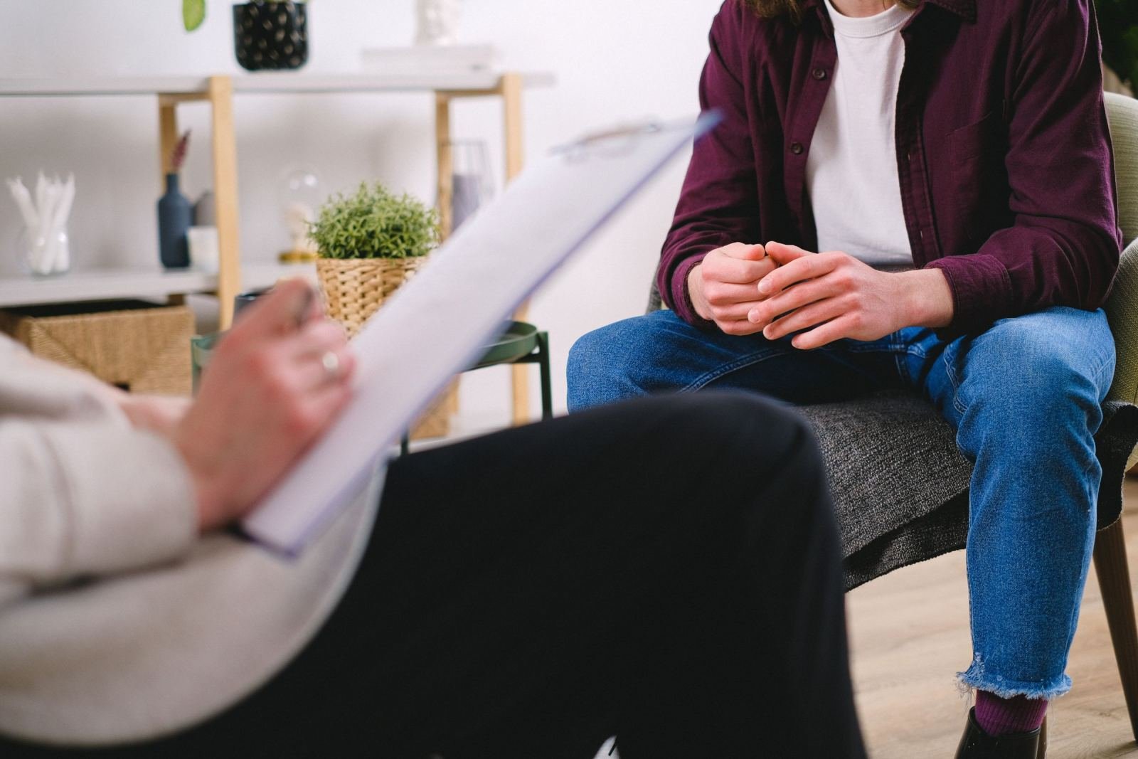 A man sits in a chair facing a therapist who is holding a clipboard