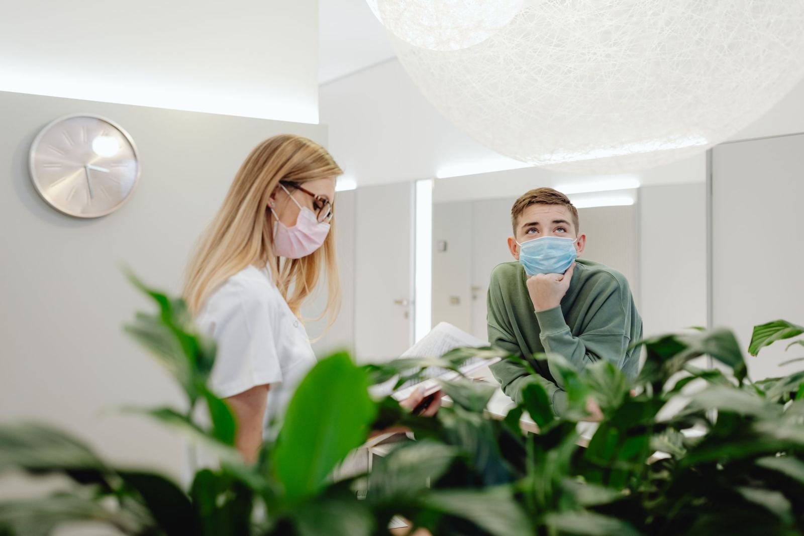 A man wearing a blue mask speaks with a medical professional in a pink mask
