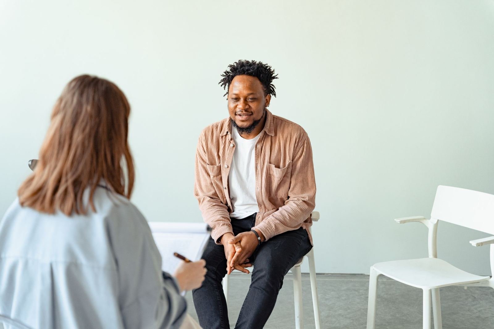 A man sits in a white chair talking with a counselor in a bright room