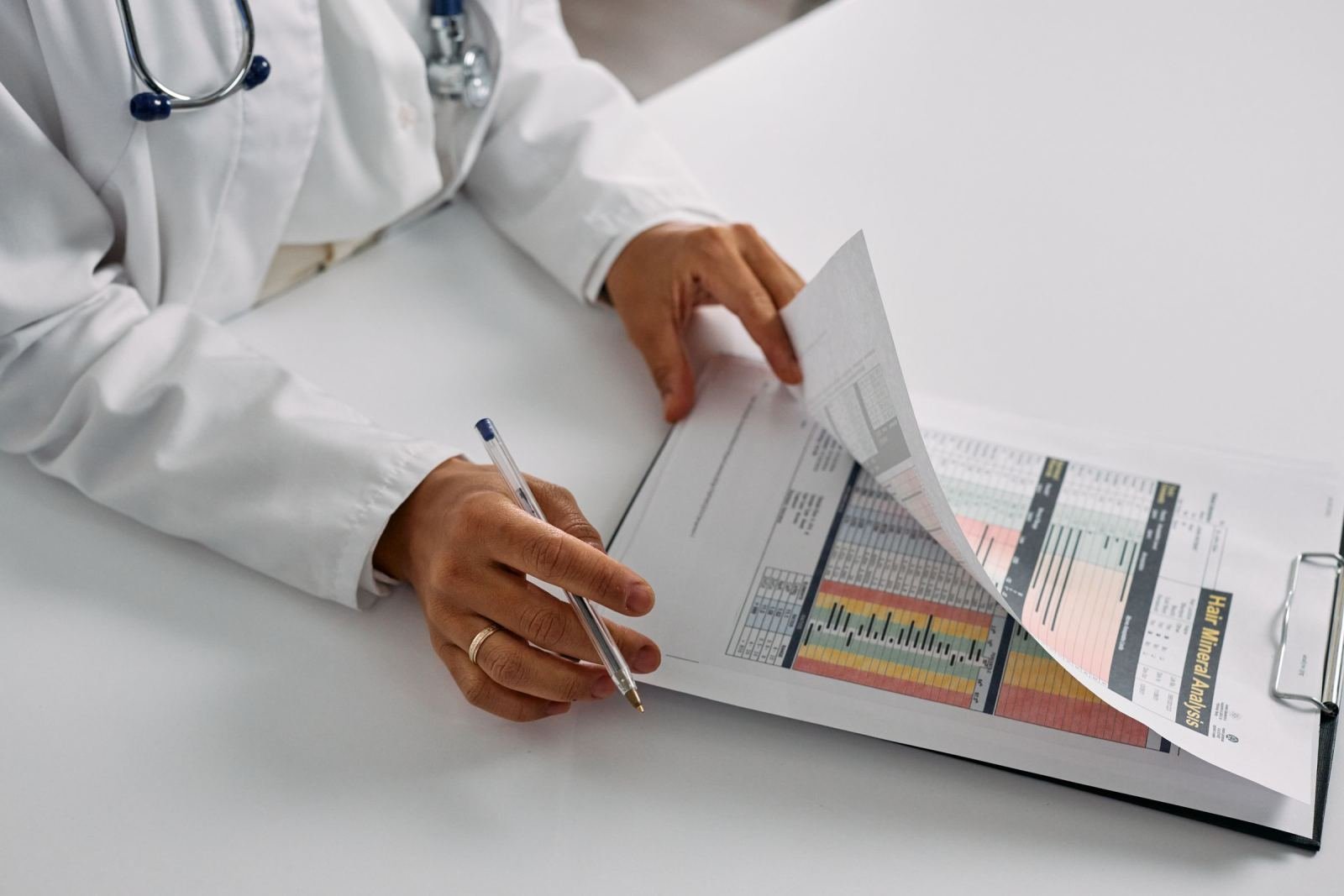 A clinician in a white coat checks a medical report held on a clipboard