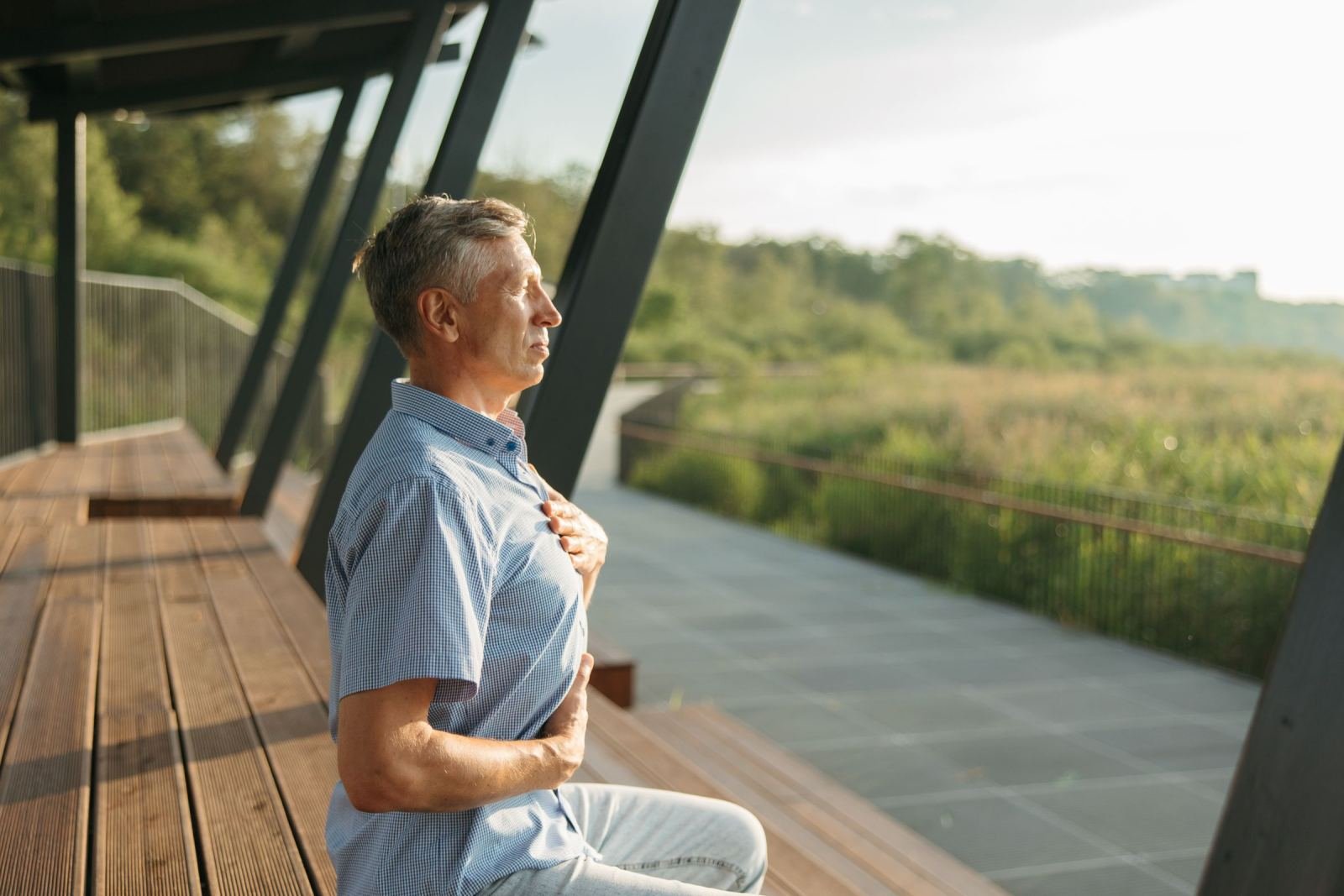 A man rests on a wooden bench, eyes shut, one hand placed on his chest.