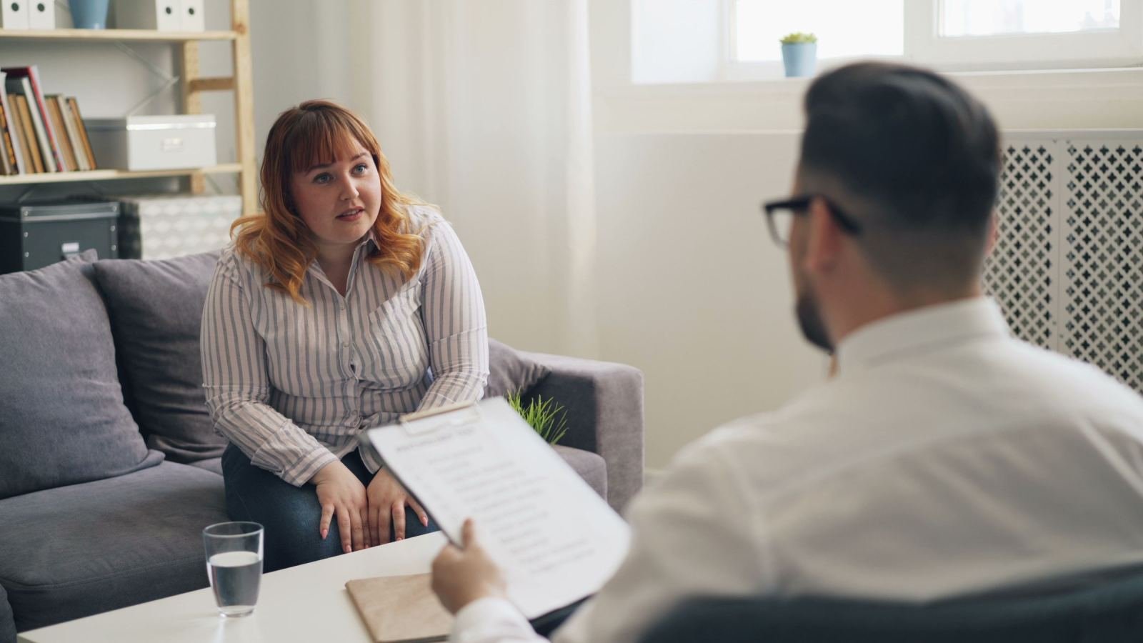 A woman speaks with a professional holding a clipboard in a bright office