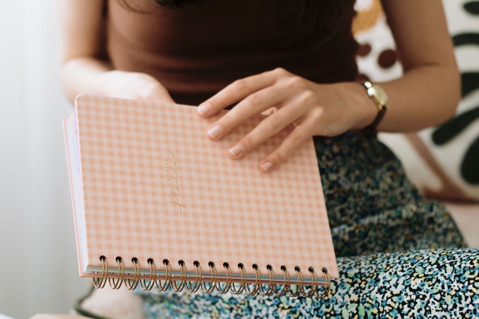A person sits with a pink checkered spiral notebook on their lap.