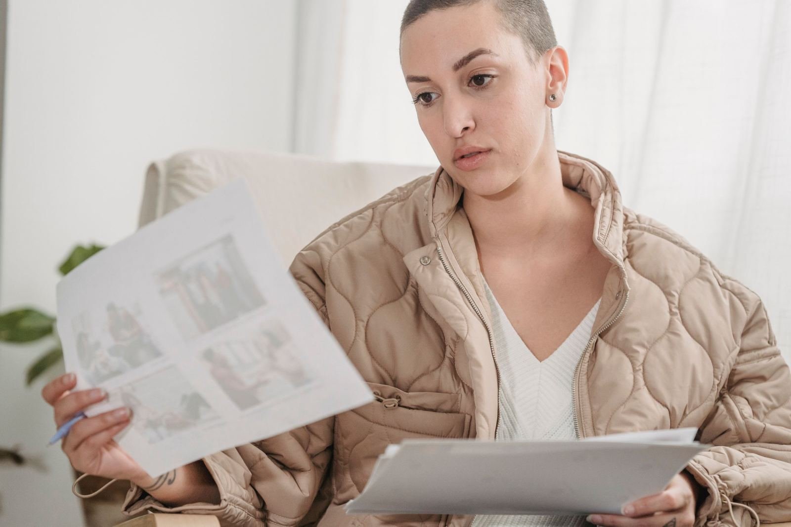 A woman wearing a tan jacket looks over papers in a well-lit room.