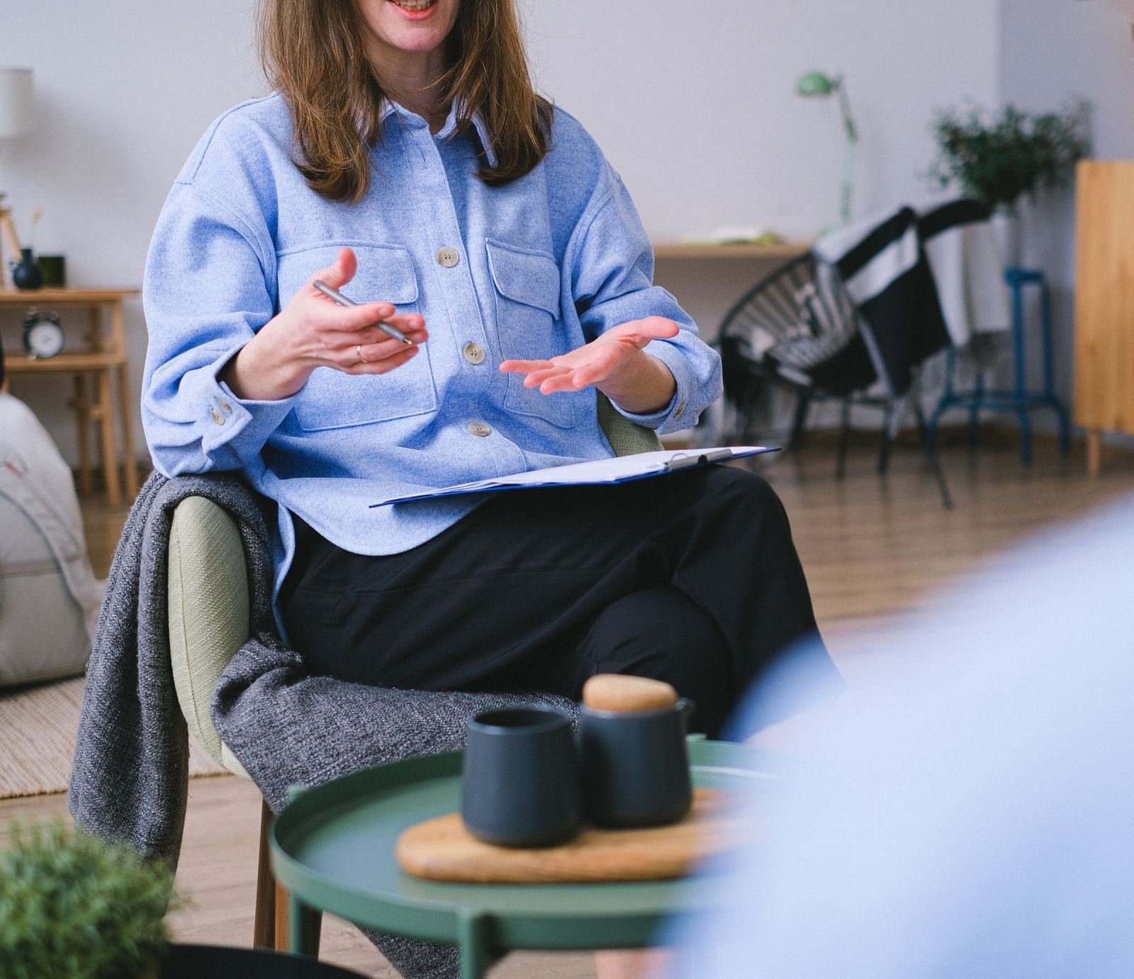 A woman in a blue shirt gestures while holding a pen and a clipboard