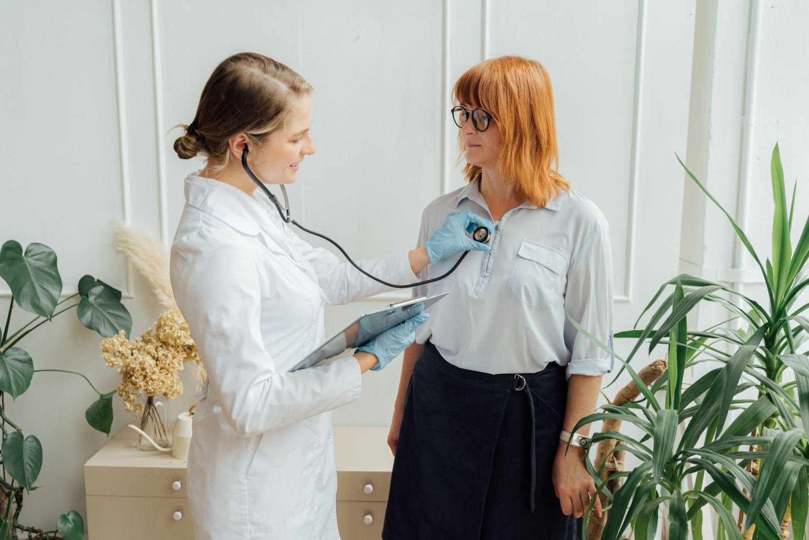 A doctor in a white coat uses a stethoscope to examine a patient