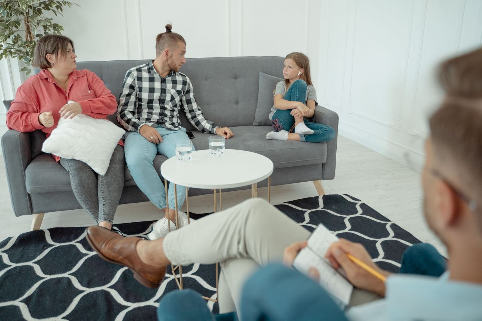 A counselor writes notes while a family of three sits on a couch