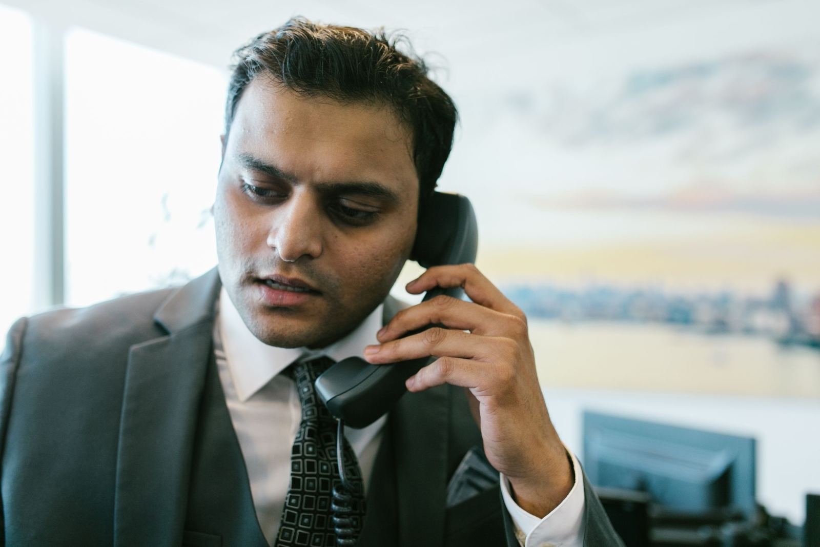 A man in a suit talks on a corded telephone in an office