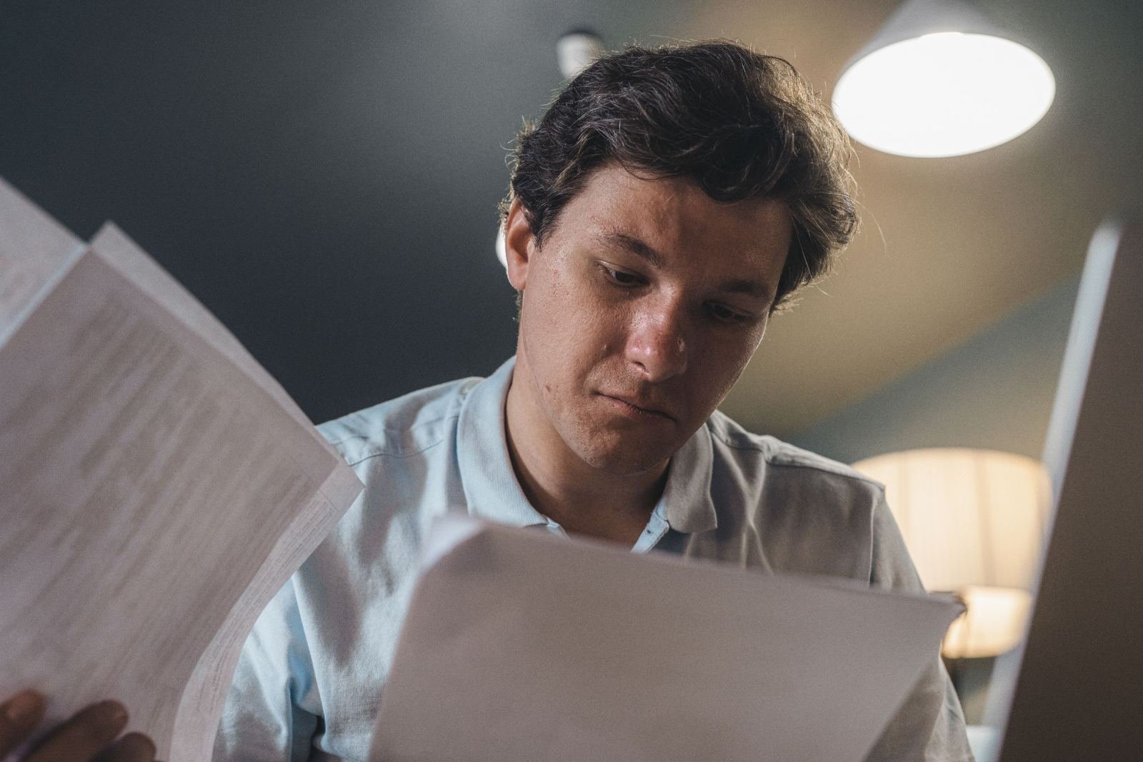 A man in a light blue shirt reads printed documents