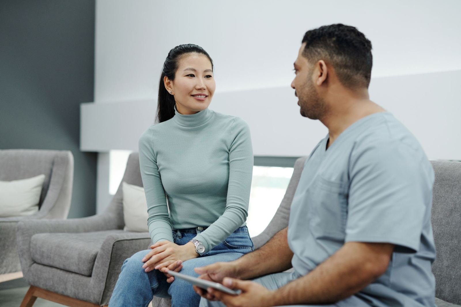 A woman in a green shirt talks with a healthcare provider in blue scrubs