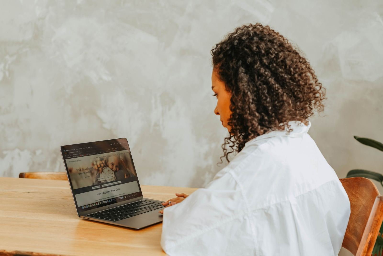 A woman wearing a white shirt works on a laptop at a wooden table
