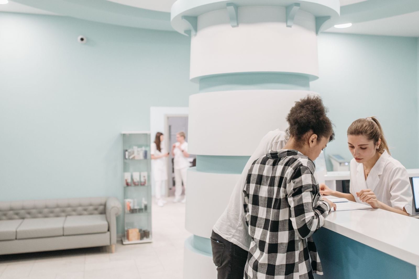 Two people speak with a staff member at a clinic reception desk