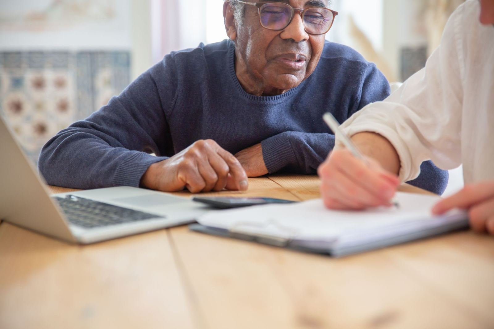 A man watches while someone fills out a form on a wooden table.
