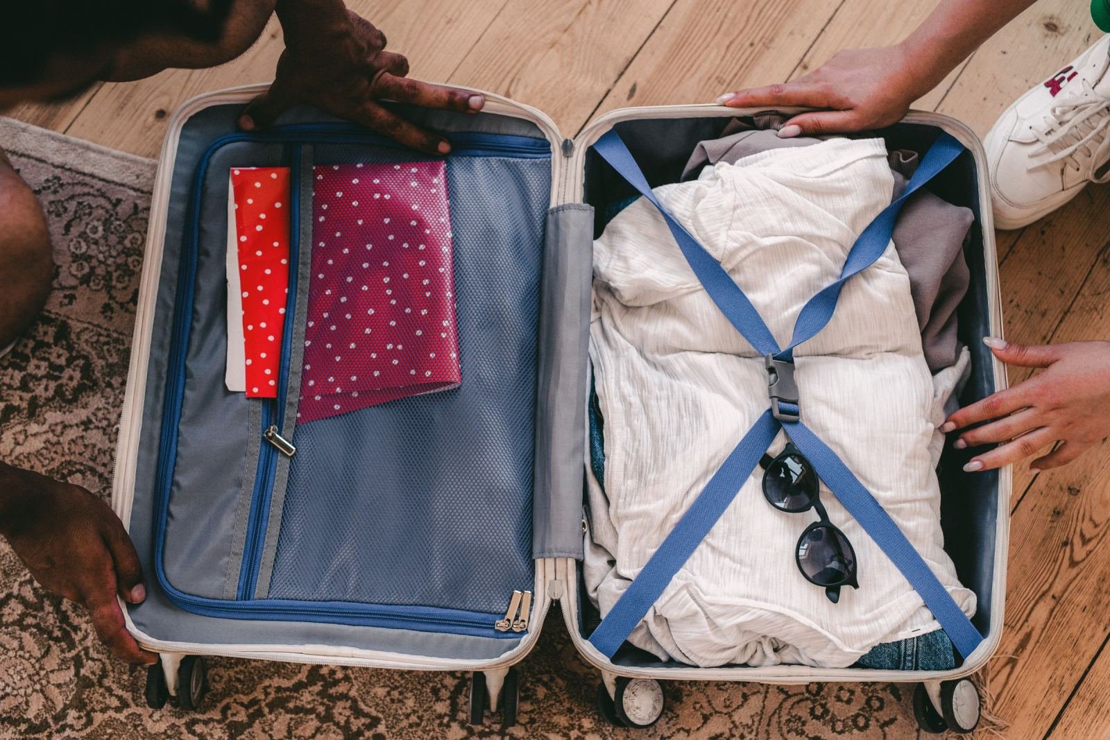 An open suitcase on a wooden floor being packed with clothes and notebooks