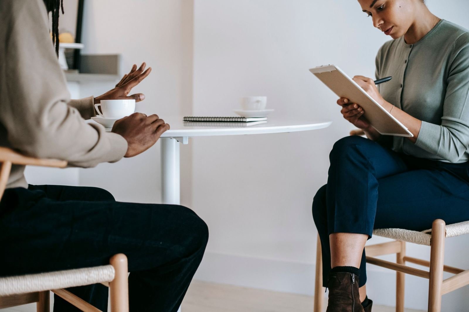 A woman with a clipboard takes notes while talking with a person in a bright room