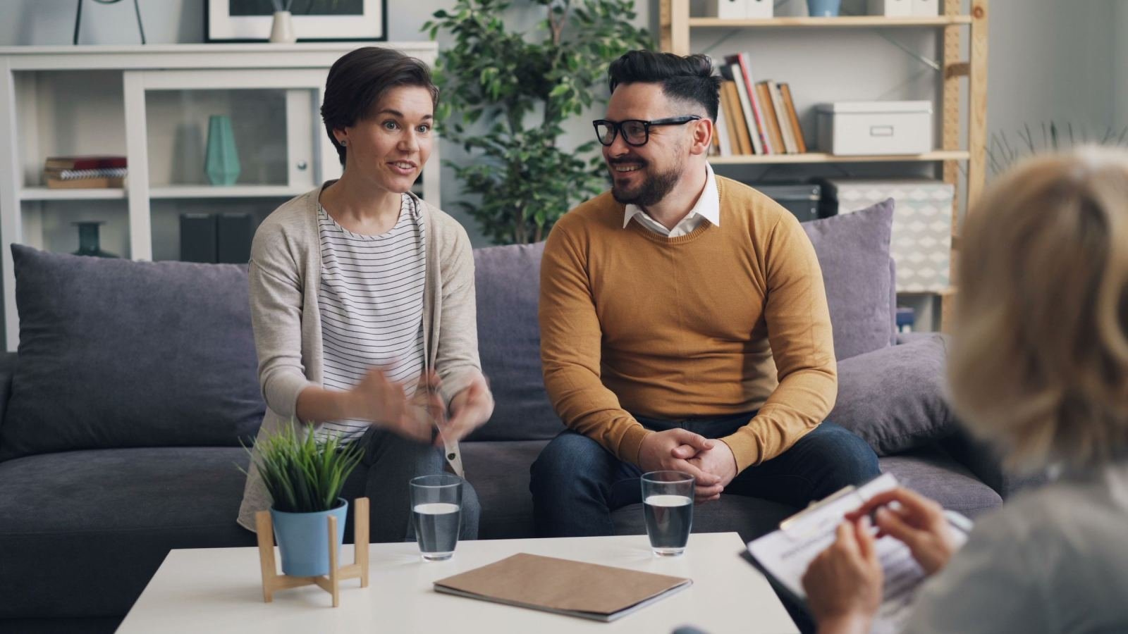 A pair of people chat with a therapist in a bright, modern room.