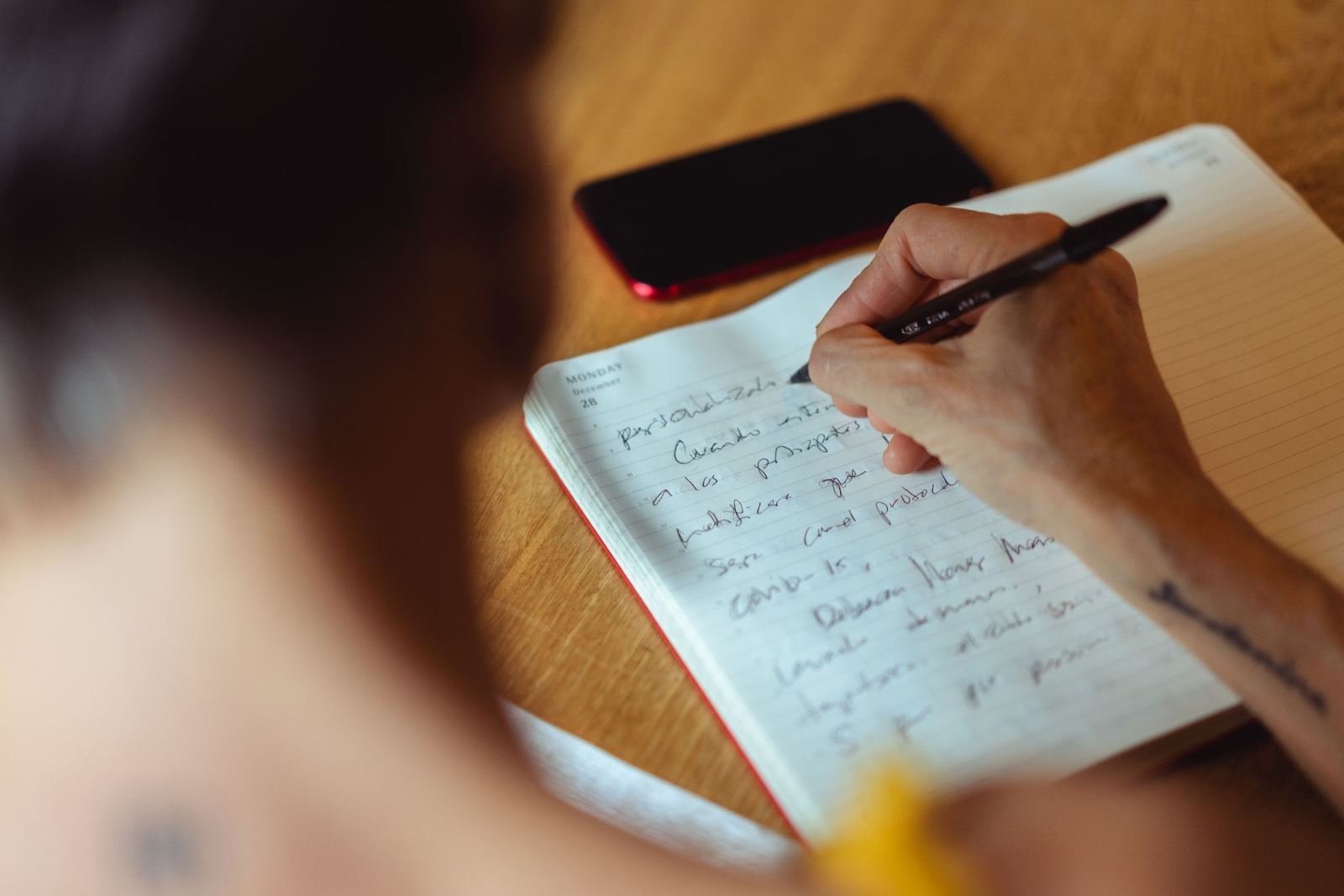 A person writes notes in a notebook with a smartphone nearby
