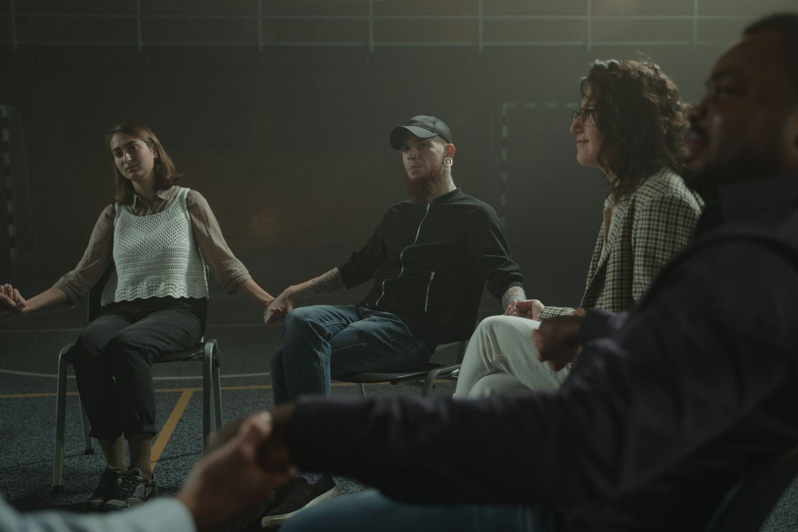 Four people sitting in a circle and holding hands in a dim room