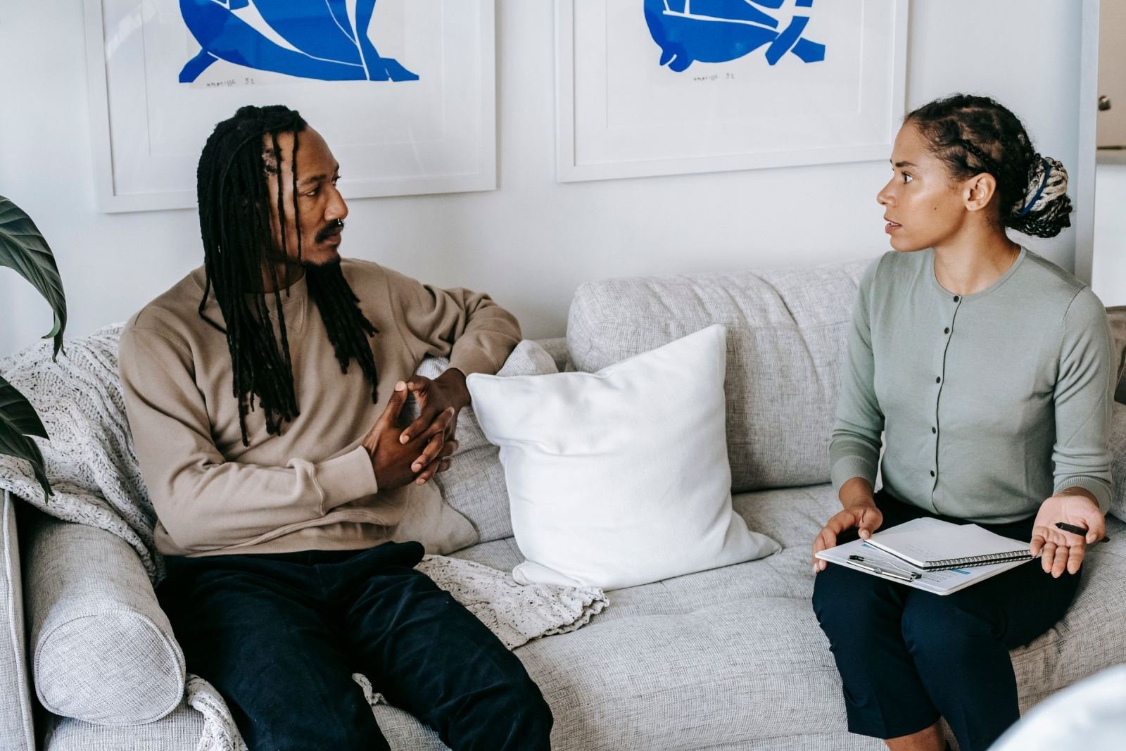 A man and a woman with a notebook sit on a sofa and talk in a bright room