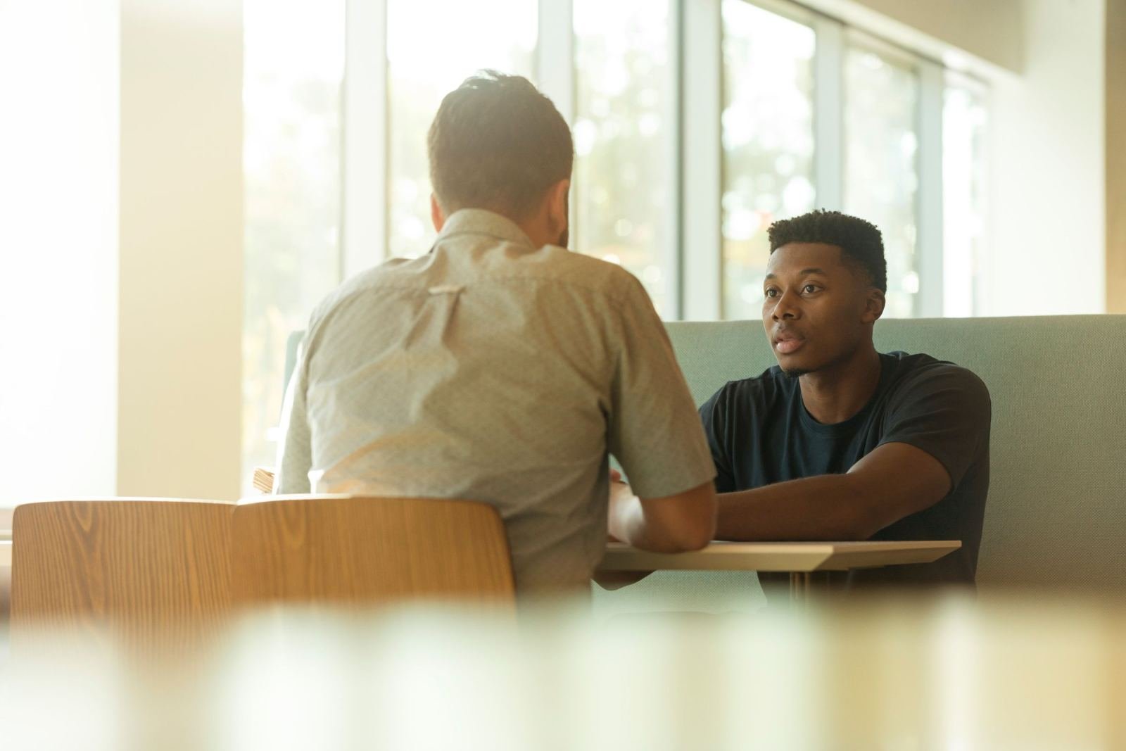 Two men sit across from each other at a table in a bright room