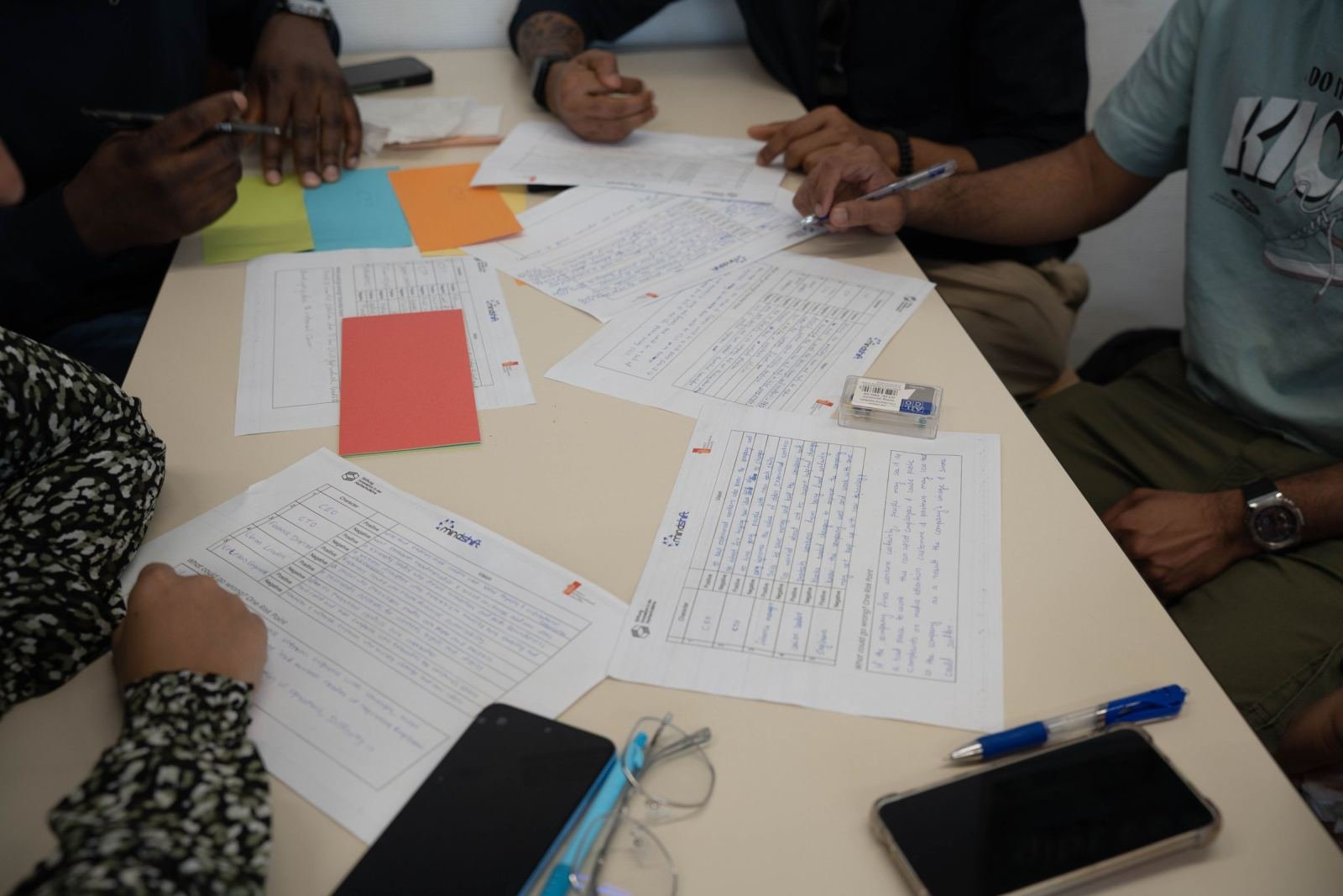 On a white table, three people look over paperwork and a hand-written list.