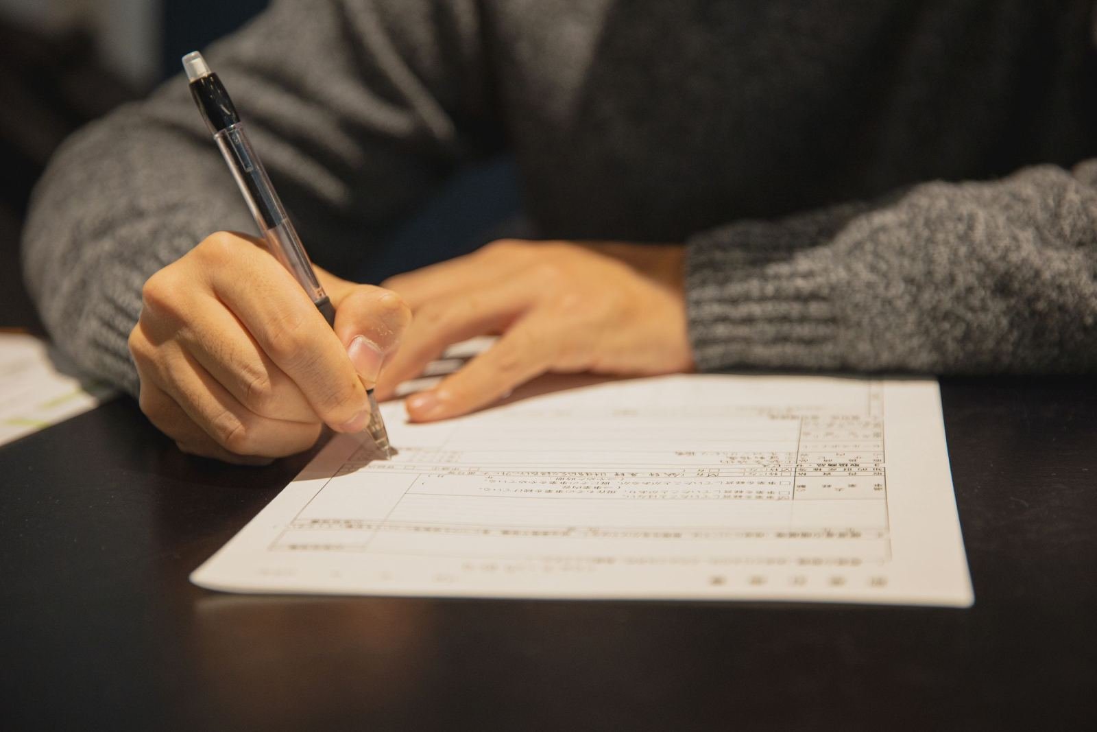 A person in a grey sweater fills out a printed form with a pen