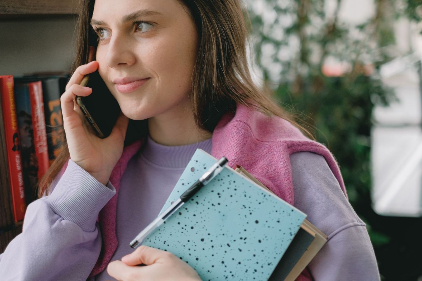 A woman holds a pen and blue notebook while talking on her phone