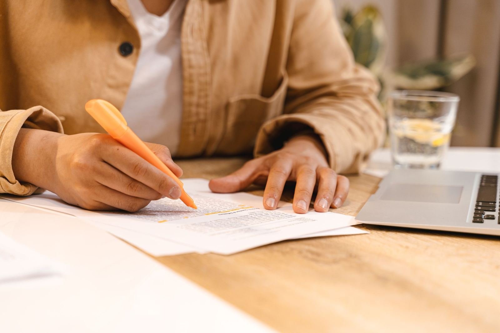 Someone highlights text on a paper form while sitting at a wood table.