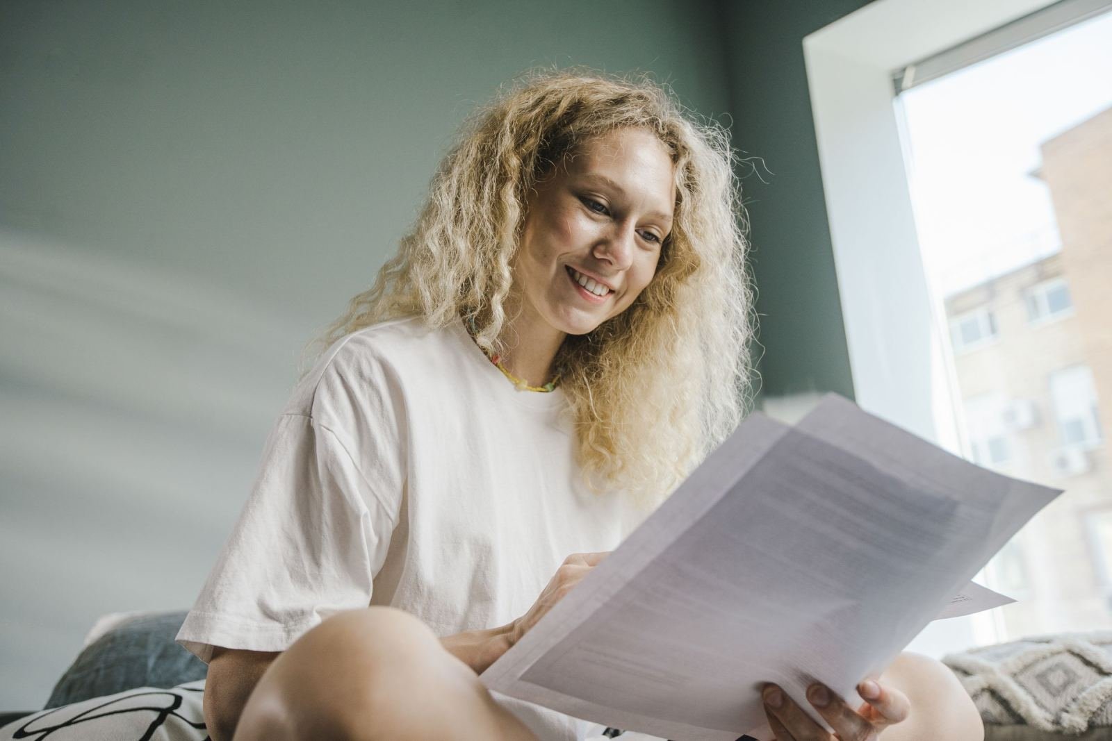 A woman with curly blonde hair smiles while reading a document