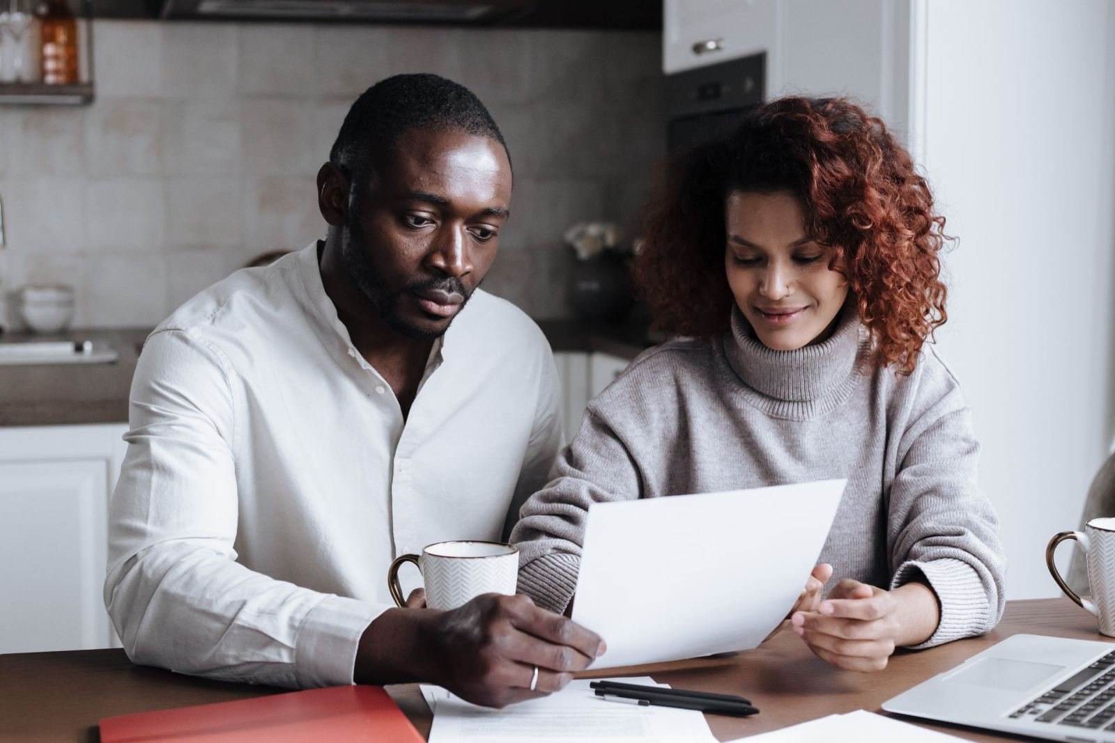 A couple sits at a kitchen table looking over a paper together.