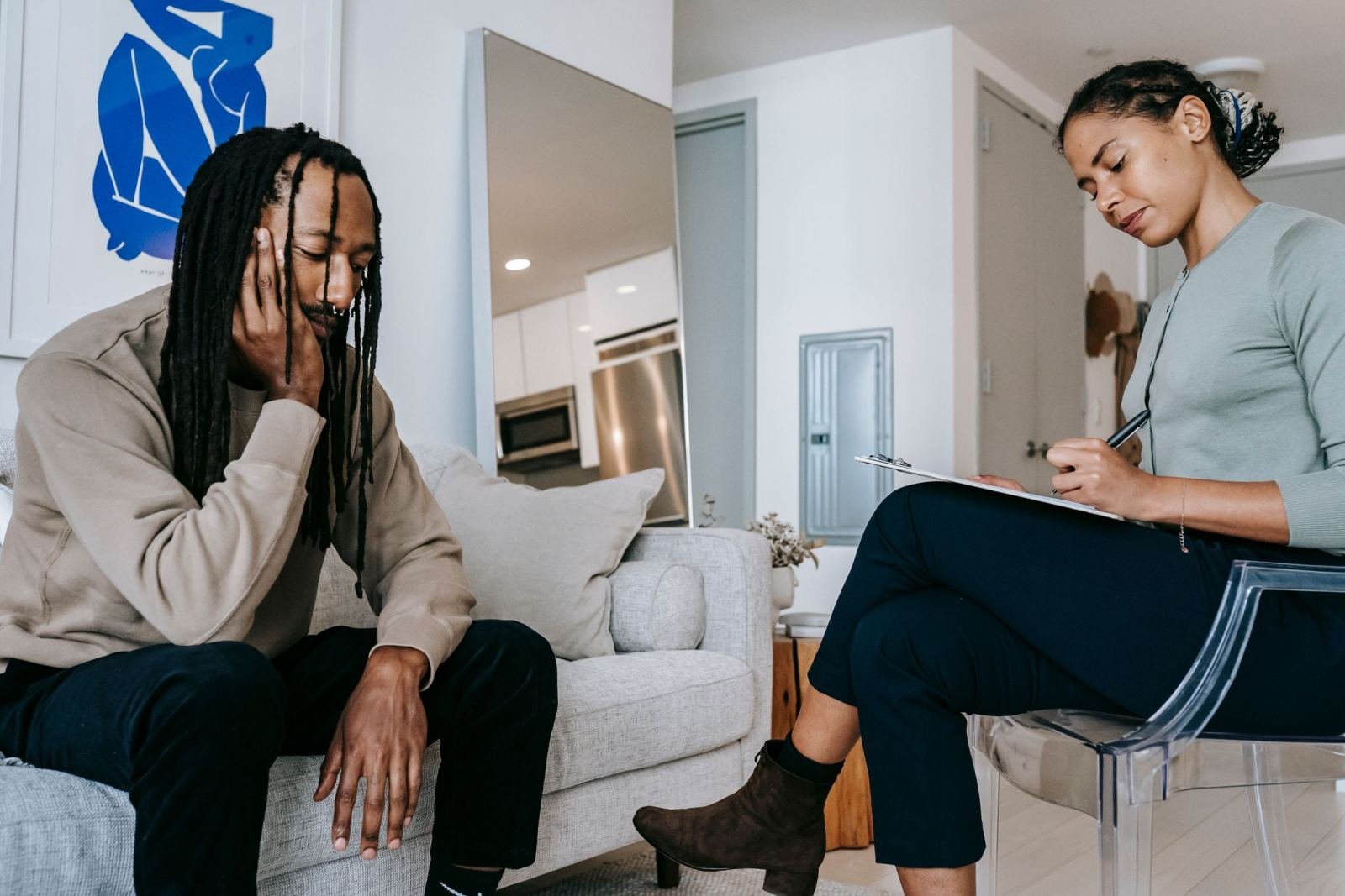 A woman writes on a clipboard while a man sits on a couch
