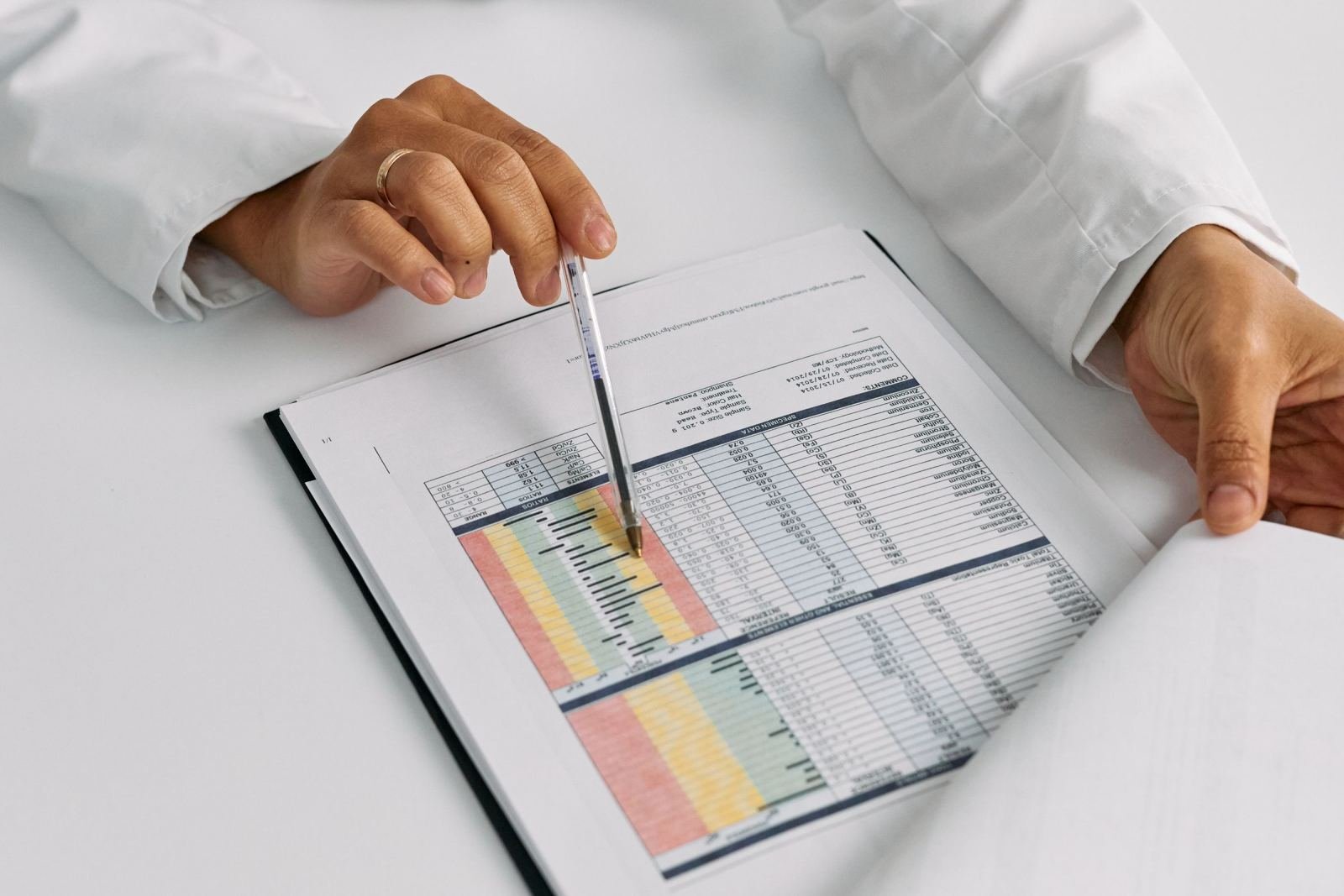 A clinician in a white coat uses a pen to point at a data table in a medical chart