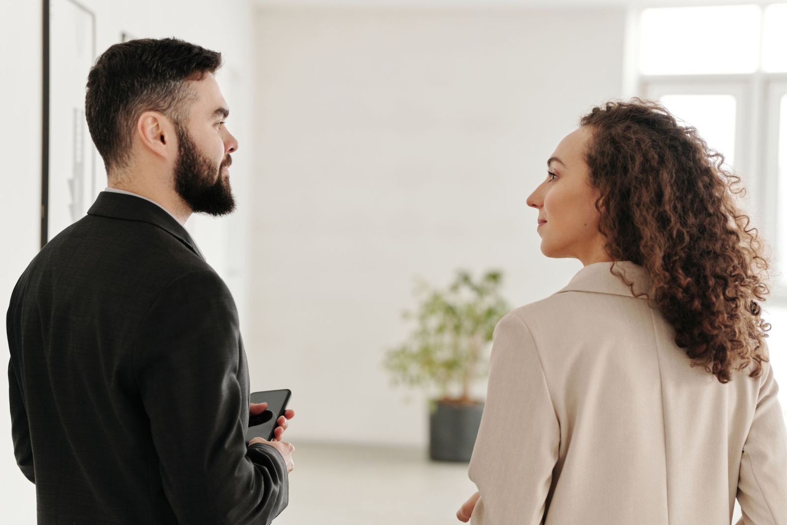 A man and a woman in professional attire stand facing each other in a bright office
