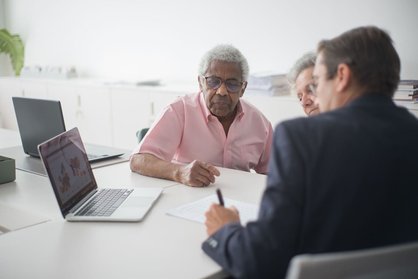 A man in a pink shirt talks to a professional in a bright room.