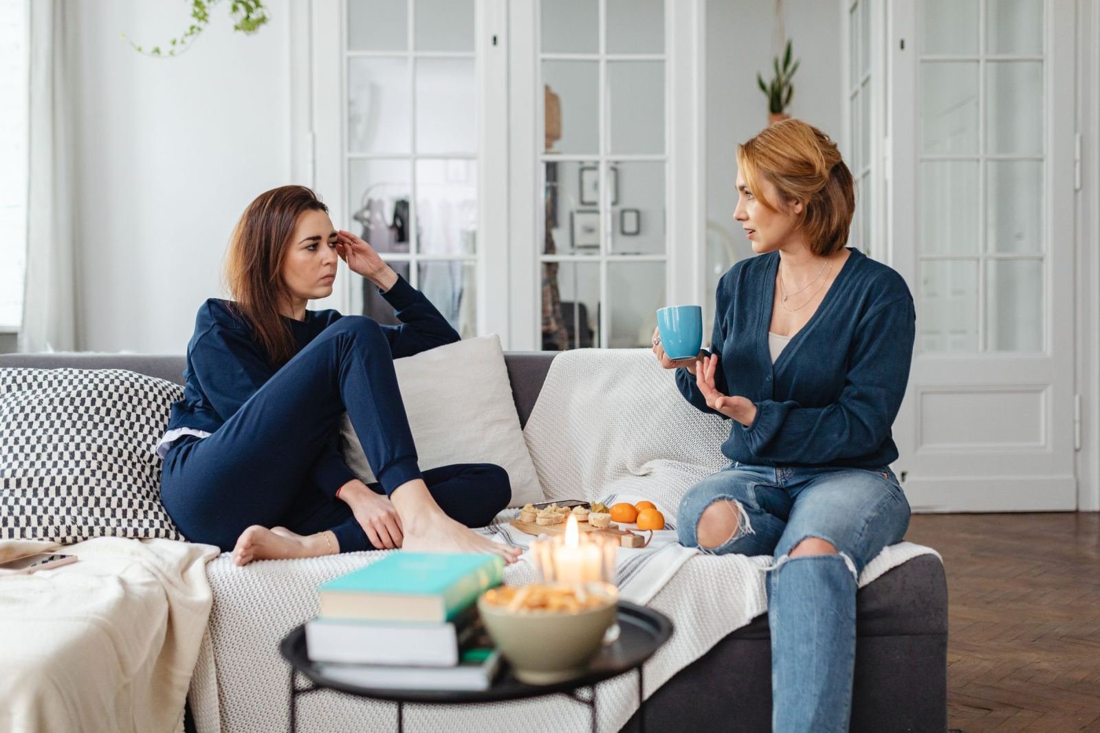 A pair of women chat on a couch, one gripping a blue cup