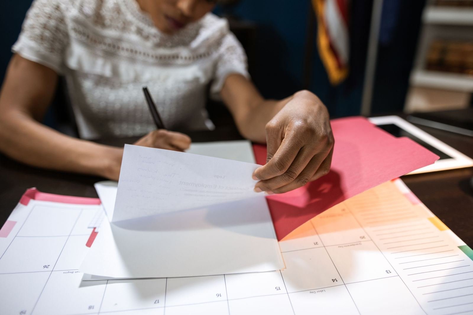 A person at a desk holding a piece of paper over a red folder and a calendar