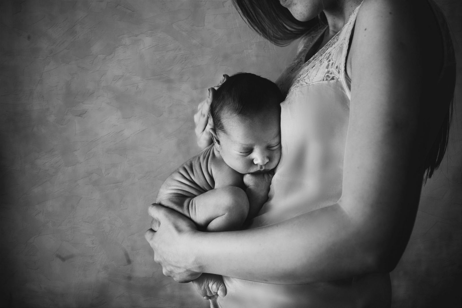A person holds a sleeping newborn baby against their chest in a black and white photo