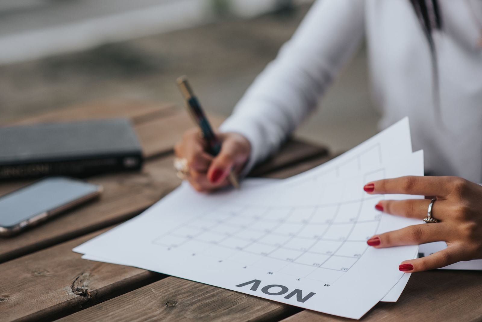 A person uses a pen to mark dates on a printed November calendar