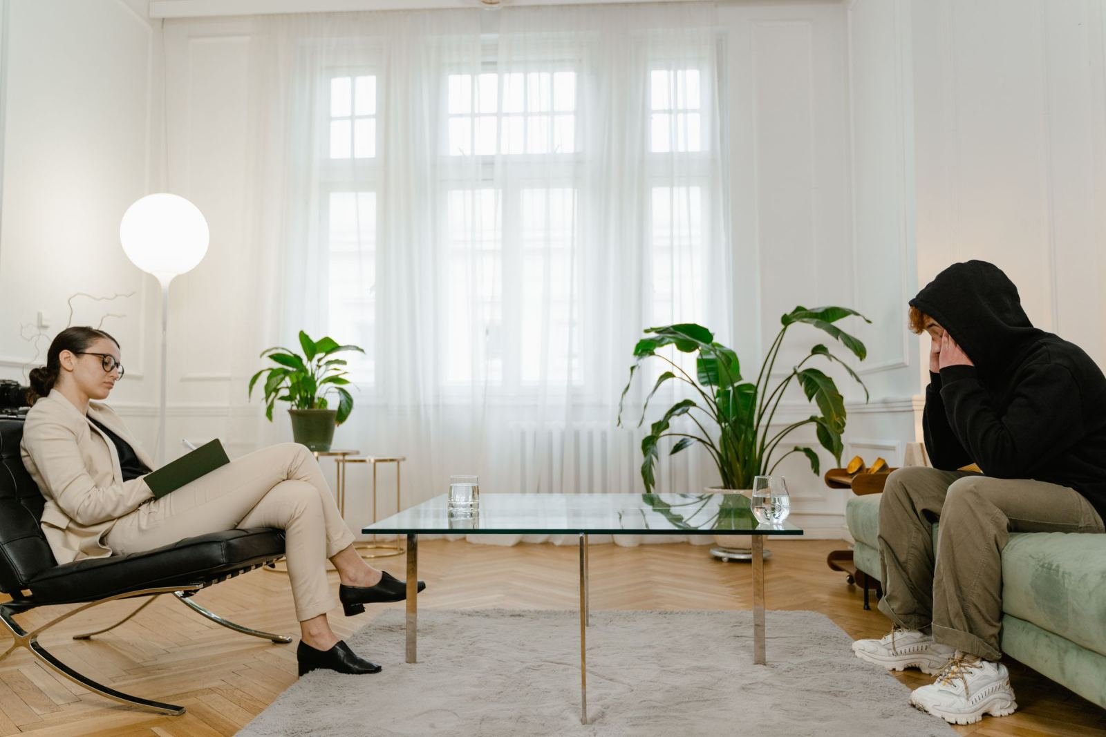 A person in a black hoodie talks with a counselor in a beige suit in a bright office.