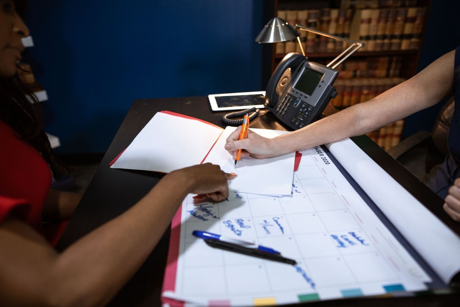 A pair of people sits at a desk, marking notes on a weekly calendar.