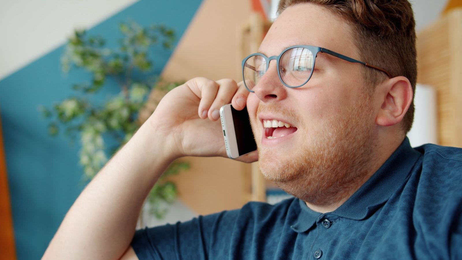 A man with glasses smiles while talking on a smartphone
