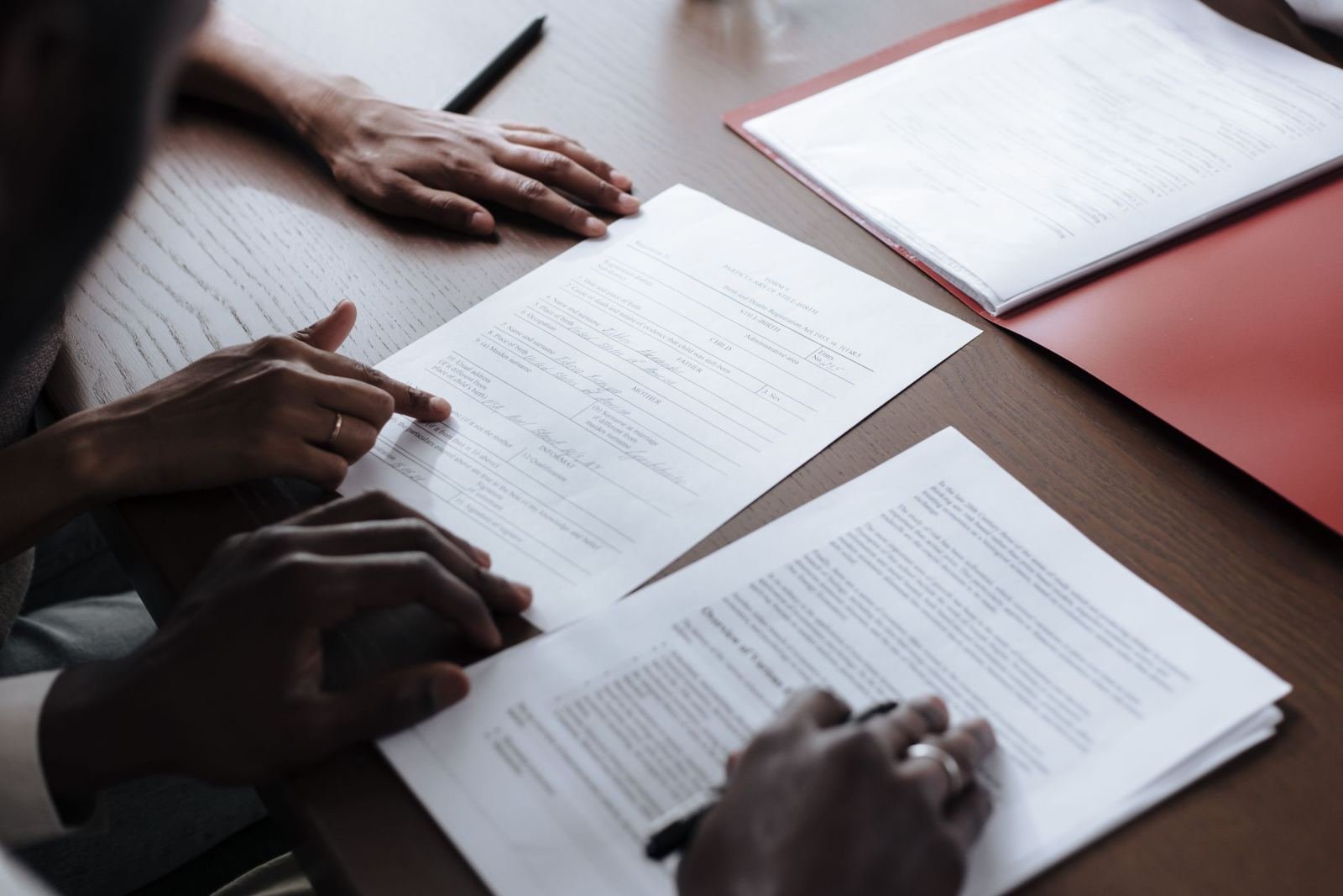 Two people sit at a wood table. They look over printed papers and point out details.