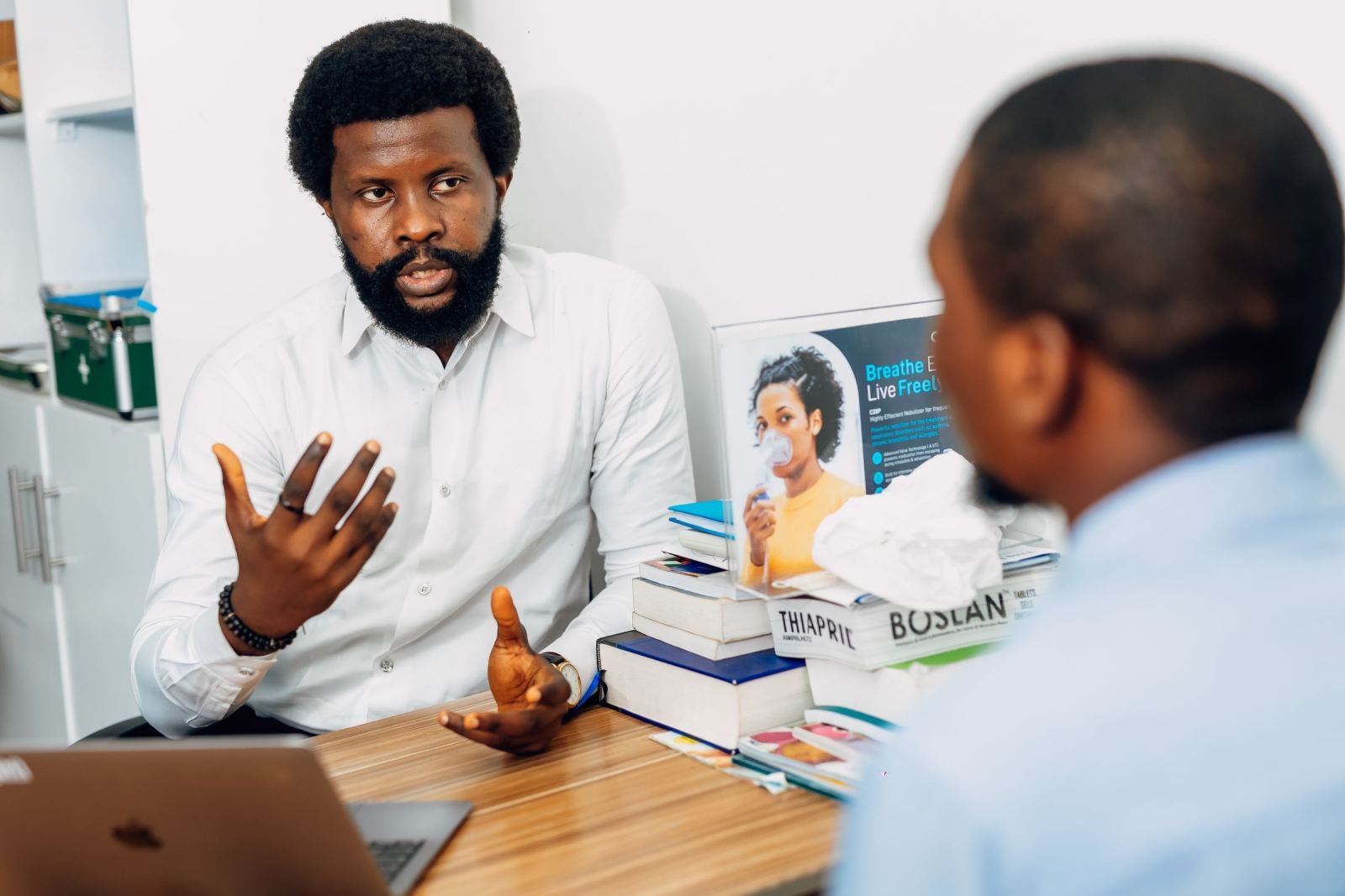 A man in a white shirt gestures while speaking to another person in a bright office