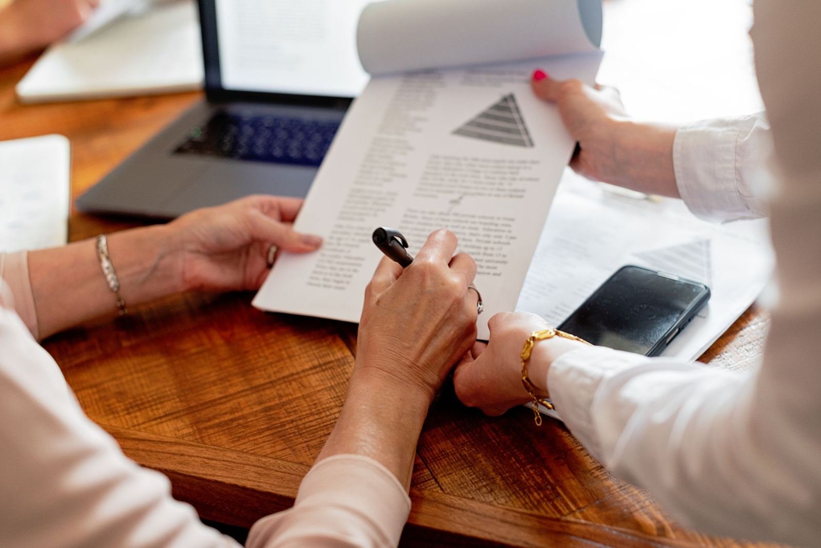 At a wooden table, two people look over a printed program plan. The plan shows a pyramid diagram.