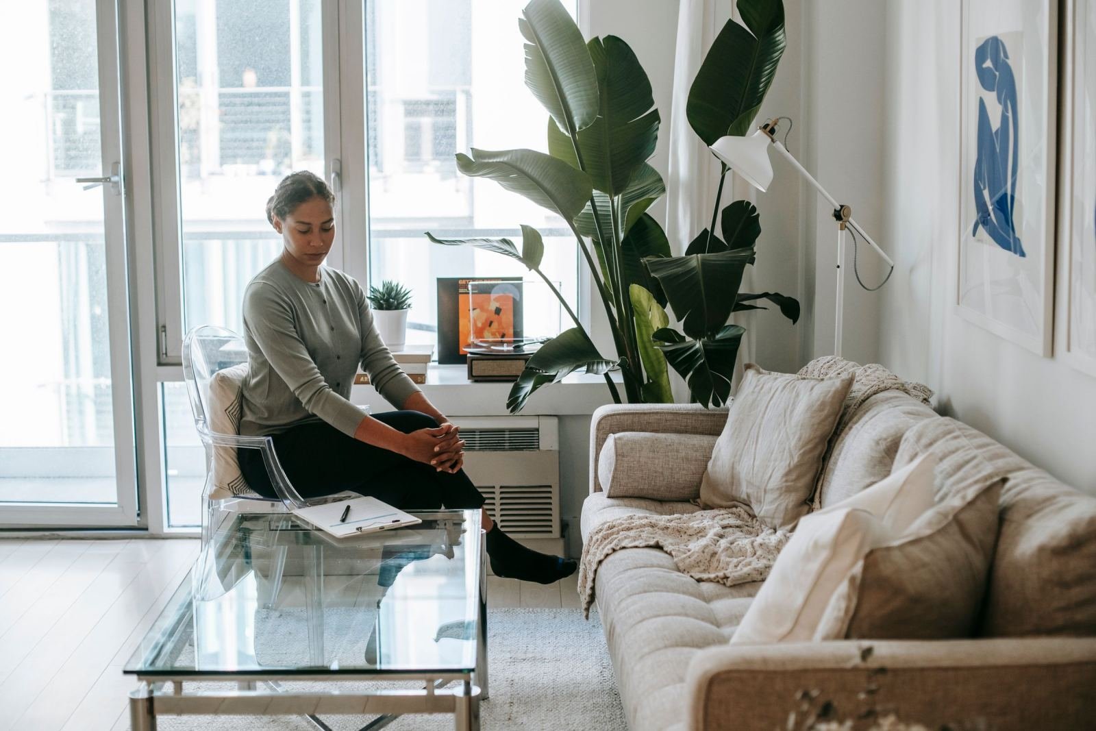 A woman sits in a clear chair looking down in a bright, modern room