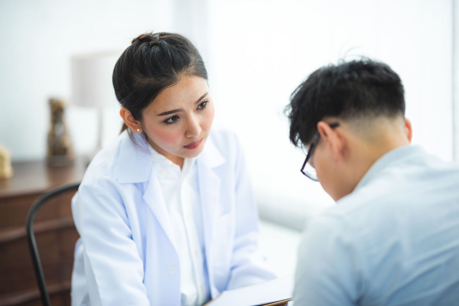 A clinician in a white coat talks with a man in a bright office