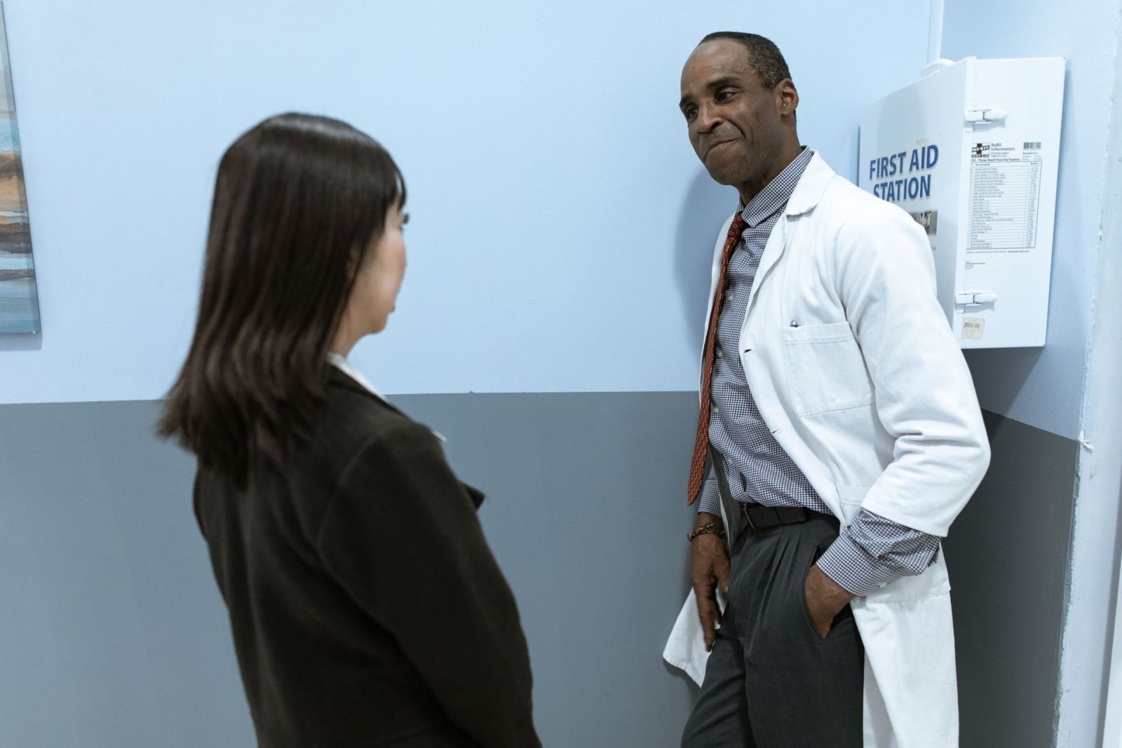 A woman sits in a medical office while a clinician in a white lab coat speaks with her